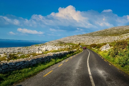 Cars on ocean road with hills, ocean and blue sky